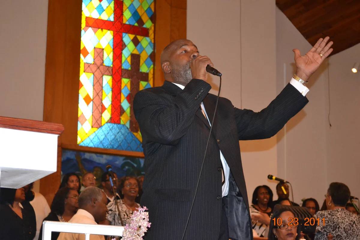 A worship leader raises his hand beside stained glass as the congregation gathers at St James.